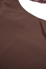 Bolso tipo morral color marrón de diseño curvo, con manija de cuerda trenzada en tonos burdeos y detalles de nudos en los extremos.
