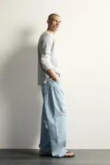 Jeans de corte barrel fit confeccionados en denim de algodón rígido, con diseño de cinco bolsillos y cierre frontal con botones. Presentan un lavado claro con efecto de roturas en las perneras.