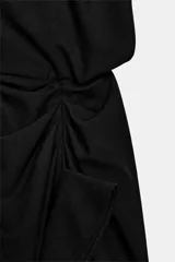 Vestido midi negro con cuello redondo y manga sisa, confeccionado por Zara Woman Collection. Presenta un diseño drapeado en la parte delantera y un bajo asimétrico con un voluminoso volante lateral. Incluye un pequeño cierre de botón en la espalda.