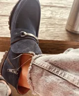 Botín de gamuza azul marino con cierre lateral y hebilla metálica decorativa.