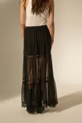 Falda larga de color negro, confeccionada en tela semitransparente con detalles de encaje en los niveles de la falda y cintura elástica.