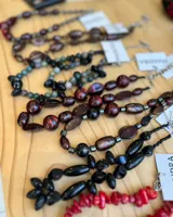 Conjunto de collares de cuentas de diferentes colores y materiales, incluyendo cuentas de piedra, madera y cristal. Los collares tienen cadenas doradas y etiquetas blancas con la marca "MANDRA".