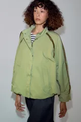 Cazadora ZARA Woman Collection color verde militar, con cuello alto, manga larga y bolsillos frontales. Cuenta con detalles de vivos a contraste en los hombros, bajo elástico asimétrico y cierre frontal oculto con cremallera y botones.