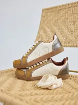 Championes de cuero con diseño de paneles en tonos crema, mostaza y detalles metalizados en el talón. Presentan cordones planos y logo bordado en el lateral.