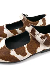 Zapato Mary Janes de cuero con estampado de vaca en tonos marrón y blanco, con correa sobre el empeine y hebilla metálica.