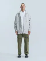 Chaqueta tipo sobrecamisa de paño color gris melange, con cuello clásico, cierre frontal con botones a presión, dos bolsillos superiores con solapa y dos bolsillos laterales. Presenta un diseño de corte recto y holgado.