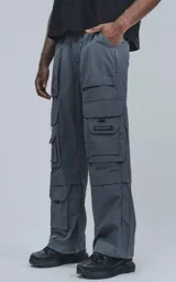 Pantalón cargo técnico gris oscuro, de silueta oversize y tejido liviano. Presenta múltiples bolsillos cargo con solapa en las piernas, uno de los cuales tiene una pequeña etiqueta negra con texto.