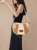Cartera bandolera de diseño semiesférico en tonos beige y arena, confeccionada con paneles de cuero y gamuza. Cuenta con un parche frontal de cuero con el logo de la marca, una correa corta para el hombro, una cadena metálica dorada decorativa y un cierre superior con tirador de cuero.