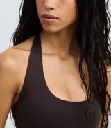 Body de poliamida color marrón oscuro, con diseño de escote halter y espalda abierta. Presenta breteles anchos que se unen alrededor del cuello y cierre inferior con botones de presión.