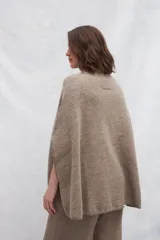 Poncho color crema de tejido de punto industrial con cuello alto y aberturas laterales para los brazos.