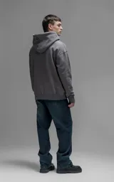 Hoodie oversize color gris oscuro, confeccionado en frisa premium con textura gamuzada. Presenta capucha ajustable con cordones personalizados, bolsillo frontal tipo canguro y puños con abertura para el pulgar.