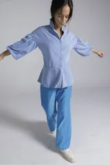 Camisa de manga larga abullonada con cuello mao y detalle de volados. Presenta un corte peplum y cierre frontal con botones.
