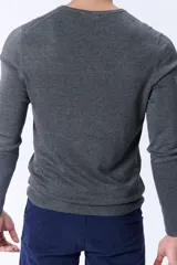 Buzo de punto en color gris oscuro, con cuello redondo y mangas largas. Presenta puños y ruedo acanalados para un ajuste cómodo.