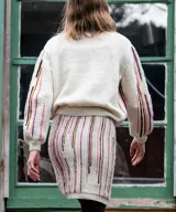 Cárdigan blanco de lana merino tejido en punto jersey, con diseño de rayas verticales bordadas a mano en tonos pasteles en el frente y las mangas. Cuenta con cuello redondo y cierre frontal con botones al tono.