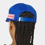 Gorra azul marino con visera curva y cierre ajustable en la parte posterior. Cuenta con un escudo bordado en hilo blanco en la parte frontal con la inscripción "EMESTUDIOS".