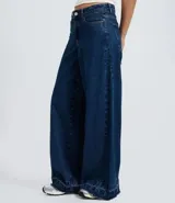 Pantalón de jean azul oscuro con corte super wide leg, cintura media, bolsillos funcionales y ruedo deshilachado.