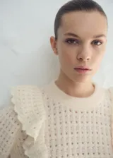 Sweater de punto color crudo, con cuello redondo y volados aplicados en los hombros.