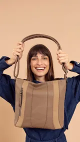 Cartera bandolera color marrón con detalles en gamuza. Tiene correa regulable, cierre metálico frontal y trasero, y división interna.