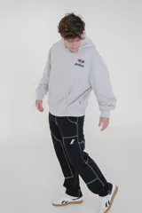 Canguro gris oscuro con efecto lavado (acid wash) y capucha. Presenta un pequeño estampado frontal con estrellas y la palabra "pulau" en tonos rosado y amarillo. Tiene bolsillo canguro y puños acanalados.