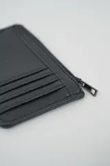 Billetera pequeña color gris claro con cierre de cremallera perimetral y tachas metálicas oscuras distribuidas en el frente.