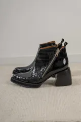 Botinetas de cuero negro con textura de reptil, diseño de punta cuadrada y taco bloque alto. Presentan cierre lateral metálico y plataforma delantera.