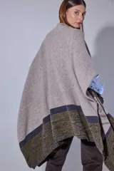 Ruana tejida en lana lambswool con diseño de bloques de color y tramas geométricas. Presenta cierre frontal con doble cursor y tiradores de cuero, permitiendo diferentes formas de uso.