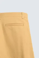 Pantalón chino straight fit de corte recto y holgado, color tostado, con pliegues frontales en la cintura, bolsillos laterales y cierre con cremallera y botón.