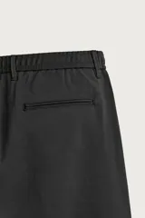 Pantalón de corte slim fit y color negro, confeccionado en tejido elástico. Cuenta con cintura elástica, trabillas, bolsillos frontales y cierre con cremallera y botón.