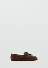 Zapato mocasín de gamuza marrón, estilo náutico, con detalles de cordones con nudo en el empeine, ojales metálicos plateados en los laterales y suela plana.