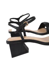 Sandalias de cuero negro con tira ancha en la parte delantera, pulsera delicada con hebilla dorada al tobillo y tacón bloque de aproximadamente 6 cm.