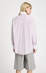 Camisa de algodón con estampado de rayas verticales en tonos rosa y blanco. Presenta cuello clásico, mangas largas con puños anchos en contraste y un detalle de pañuelo integrado en el cuello que simula una corbata. Posee cierre frontal de botones y corte recto.