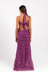 Vestido largo de encaje con patrón circular, color lila, de corte halter con tiras cruzadas al cuello y aberturas laterales en la cintura.