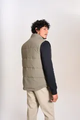 Chaleco puffer de corte regular, color beige, con cierre frontal y cuello alto. Presenta un diseño acolchado horizontal y logo bordado en el pecho.