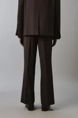 Pantalón de traje flare fit para hombre, confeccionado en tejido con lana, en color marrón oscuro. Presenta tiro medio, trabillas para cinturón, cierre frontal con cremallera y botón, bolsillos laterales y raya central marcada en las perneras.