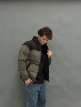 Campera puffer con capucha, diseño bicolor en verde oliva y negro, cierre frontal y bolsillos laterales.