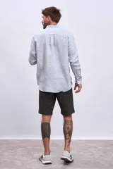 Camisa de manga larga para hombre, con cuello clásico y botones frontales. Presenta un estampado de rayas verticales finas en tonos azul claro y blanco.