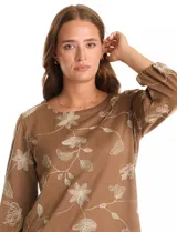 Blusa de tejido fino color marrón con bordado floral en hilo dorado. Presenta cuello redondo, mangas tres cuartos abullonadas con puños elásticos fruncidos y ruedo redondeado con corte asimétrico.