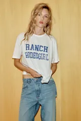 Camiseta de corte oversize confeccionada en algodón flamé, con cuello redondo y manga corta. Presenta un diseño con efecto desgastado, detalles de roturas en el tejido y estampado de texto a contraste en la parte frontal.