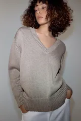 Sweater de punto grueso color beige, con cuello en V profundo y mangas largas. Cuenta con terminaciones acanaladas en el cuello, los puños y el ruedo.
