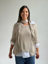 Sweater de punto fino en color beige, con cuello redondo y mangas tres cuartos. El diseño incluye una bufanda integrada del mismo tejido con detalles de puntilla en los extremos.
