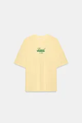 Camiseta amarilla de corte oversize, con cuello redondo, manga corta y estampa frontal en color verde con texto alusivo a Brasil Ipanema y pequeños símbolos.