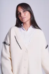 Cárdigan color beige con botones negros, escote en V y detalles de costuras bordadas en negro.