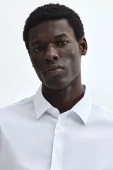 Camisa de vestir H&M de corte entallado, confeccionada en tejido elástico de mezcla de algodón. Presenta cuello italiano, cierre frontal de botones y mangas largas con puños ajustables.