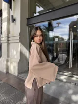 Polerón de cuello alto, color beige, con diseño holgado y mangas amplias con aberturas laterales en el ruedo.