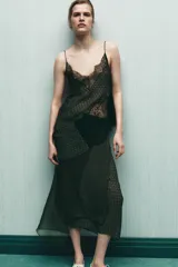 Top estampado con diseño geométrico en tonos verdes y marrones, confeccionado en viscosa 100%. Presenta escote en pico, tirantes finos y detalle de encaje negro a contraste. El bajo tiene un acabado asimétrico.