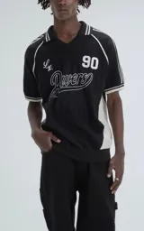 Chomba deportiva de tejido de punto con cuello polo y cierre frontal en V. Presenta diseño bicolor en negro y blanco, con detalles de rayas en hombros y mangas, y estampado frontal con el texto 'Ravers' y el número '90'.