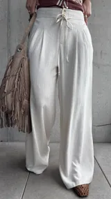 Pantalón palazo de lino color beige, de calce amplio y fluido, con tablas en el frente, botón, cierre y cordón ajustable en la cintura.