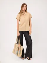 Camisa de manga corta color beige, confeccionada en mezcla de algodón y lino, con cuello camisero, cierre frontal de botones y dos bolsillos aplicados en el pecho.