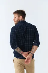 Camisa de pana a cuadros en tonos azul y bordó, de corte regular, manga larga, con cartera de botones y bolsillo frontal.