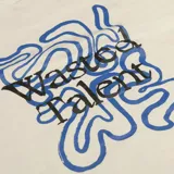 Remera de algodón color hueso con corte regular. Presenta un pequeño estampado con el texto 'Wasted Talent' en el centro del pecho y un detalle de costura en forma de 'W' en la manga izquierda.